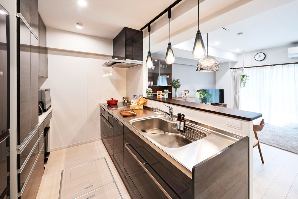 ダークな木目調の扉とステンレスワークトップが印象的な、ペンダントライトのある対面式キッチン